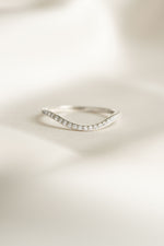 Silver curved ring with small diamonds on a light beige background