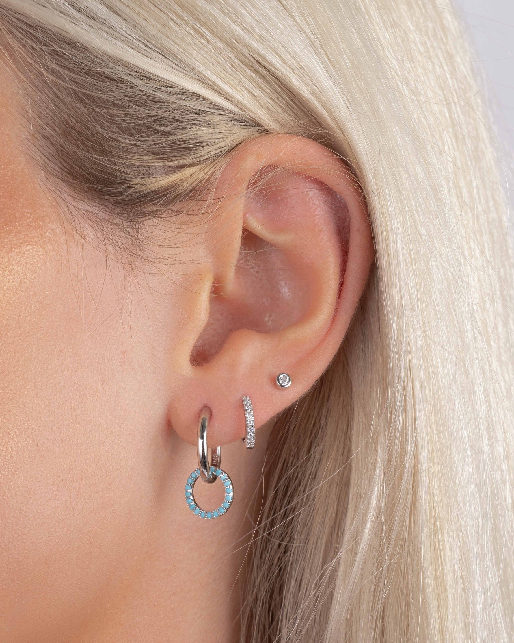 Close-up of a person wearing sterling silver hoop earrings with a dangle earring design and turquoise stones, paired with dainty silver earrings