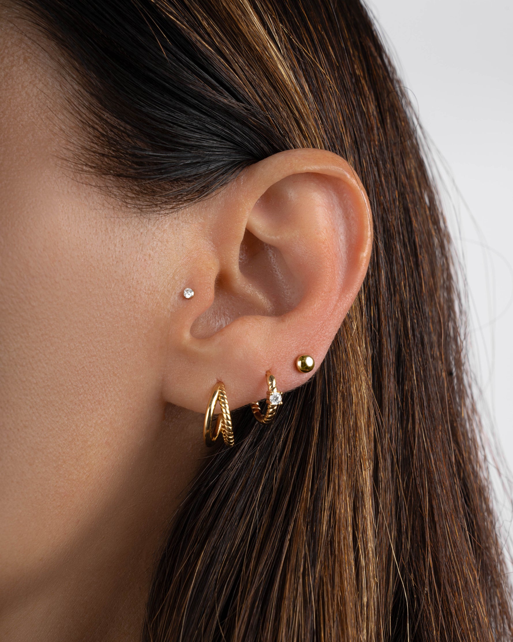 Model wearing gold textured hoops, gold spiral diamond hoop and gold stud earrings 