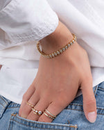 model wearing a gold bypass ring, gold diamond ring set, and a dainty stacking ring, paired with a gold oval bezel set diamond tennis bracelet
