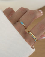 model wearing gold thin band stacking rings, one turquoise baguette gemstone ring, one gold dainty ring, and one turquoise ring with an eternity band