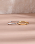 Two gold and sterling silver stackable rings on a soft pink fabric background