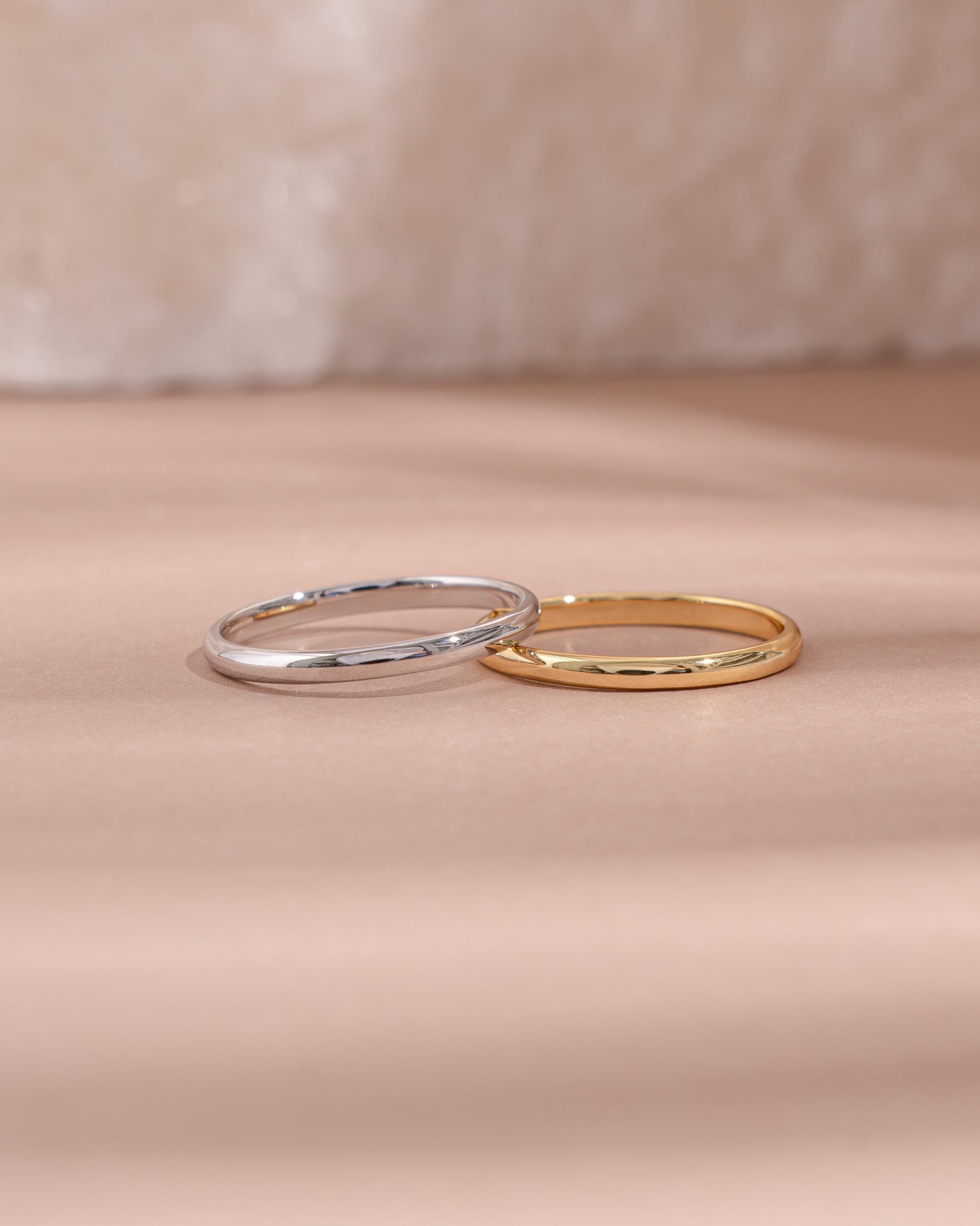 Two gold and sterling silver stackable rings on a soft pink fabric background