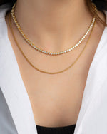 Two gold layering necklaces on model featuring a tennis necklace and a gold box chain necklace 