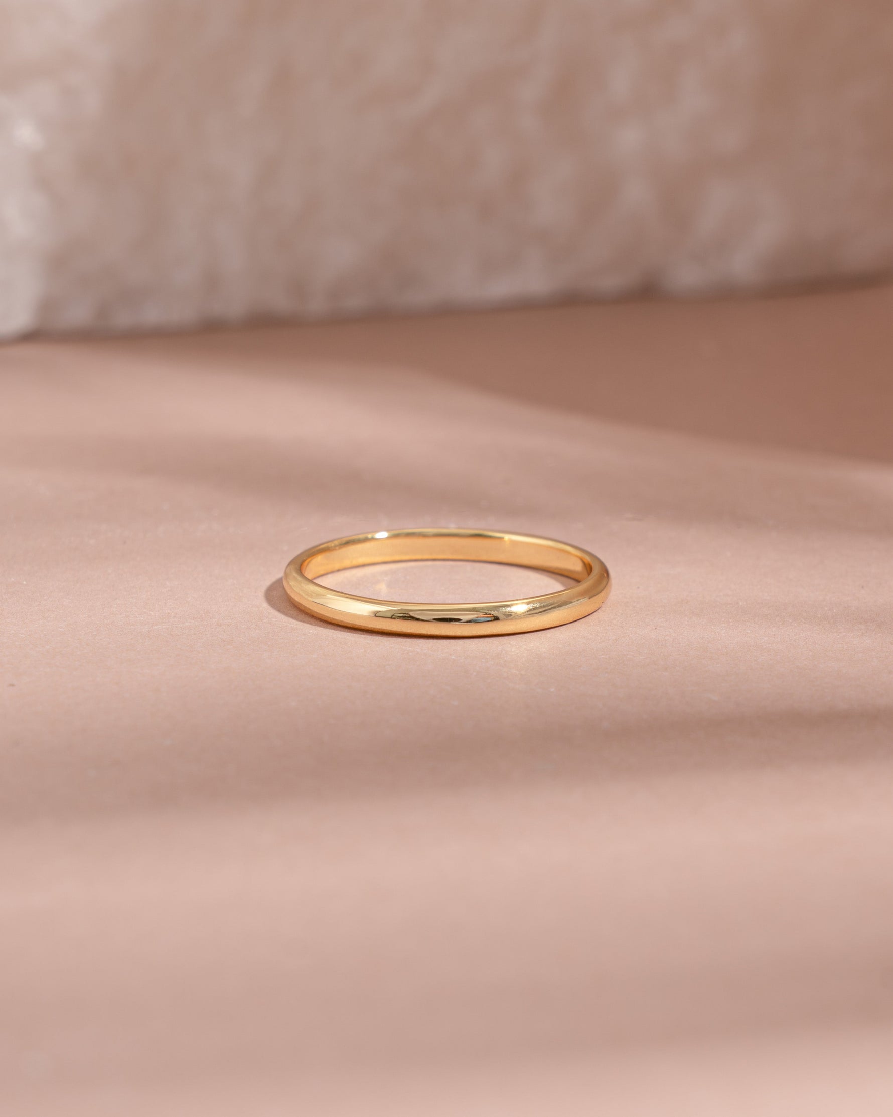 Gold stacking ring on a soft pink fabric background
