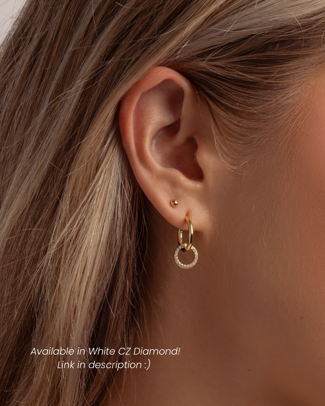 Close-up of an ear wearing a gold charm hoop earring with a dainty ball stud earring