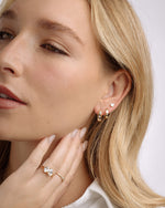 Model wearing celestial jewelry featuring diamond tiny hoop earrings, dainty huggie earrings, a pear cut diamond stud earring and gold diamond stacking rings