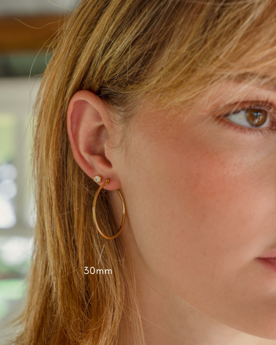 closeup image of model wearing 30mm gold hoop earrings and bezel stud earring