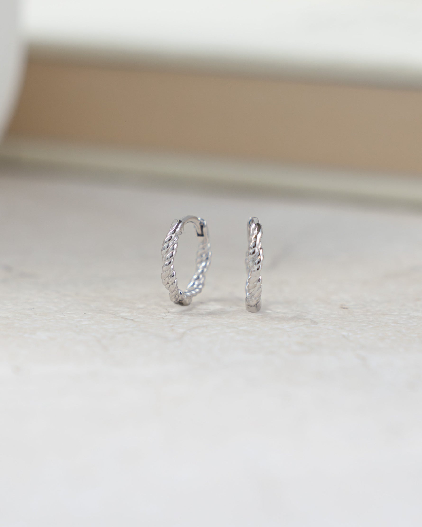 Silver hoop earrings  with rope earring design on a light wooden surface