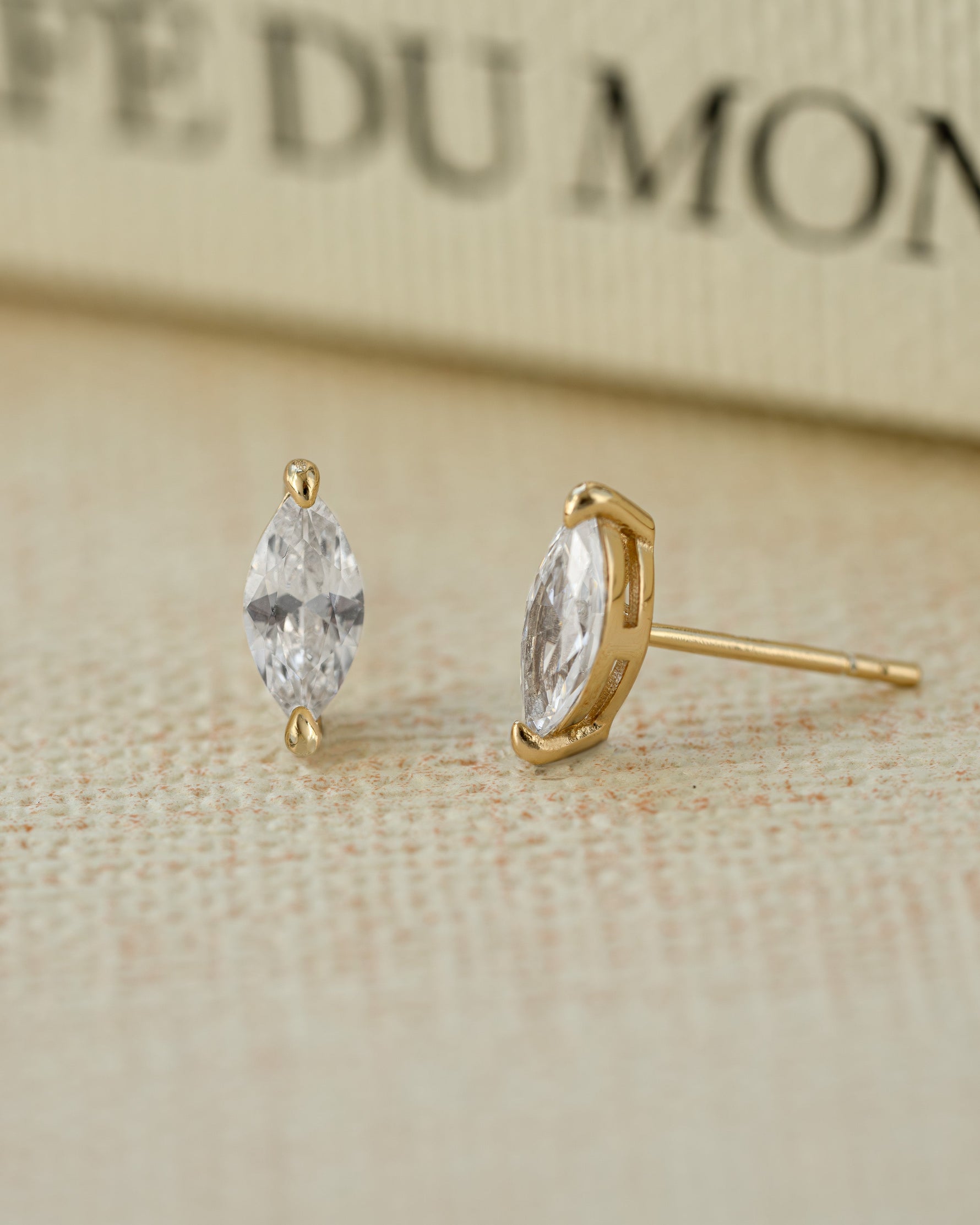 Gold plated diamond earrings on a beige background