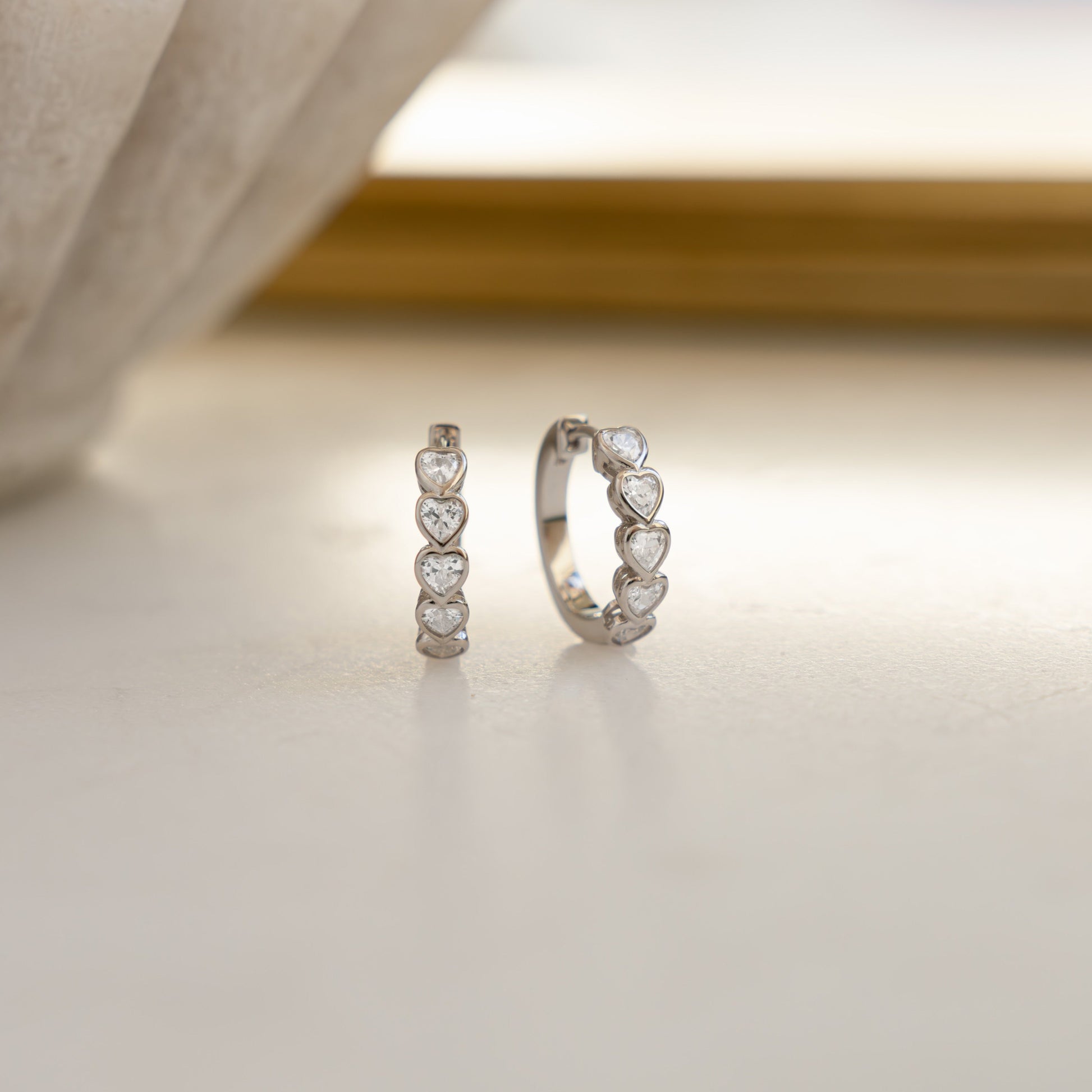 Close-up of bezeled heart hoops, showcasing its intricate design and shimmering diamond gemstones.