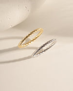 Two rings on a beige surface, one in 14k gold plating featuring a spiral design and one in 925 sterling silver