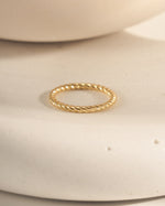 Gold textured stacking ring on a white ceramic surface