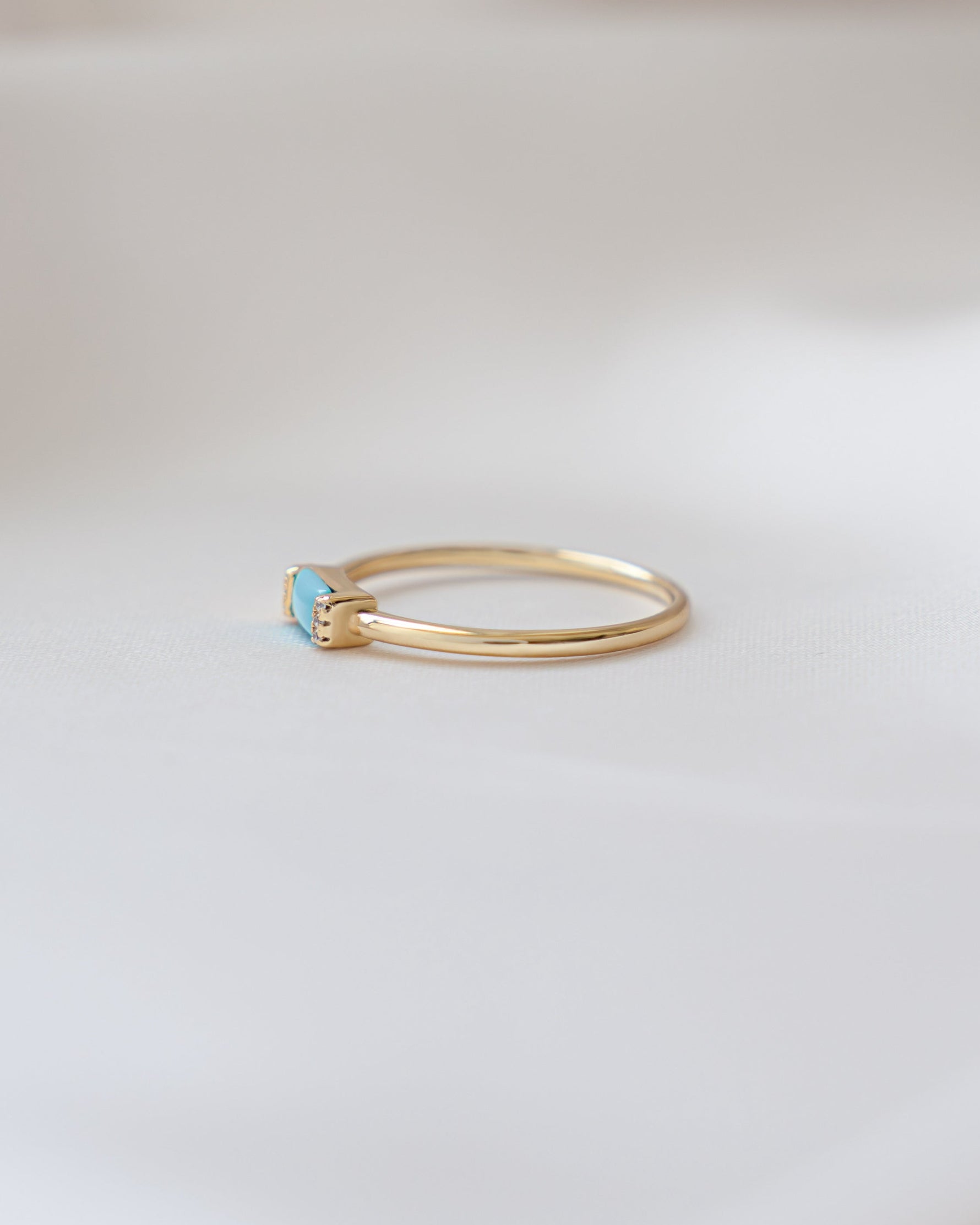 Thin gold ring with a baguette turquoise gemstone on a light background