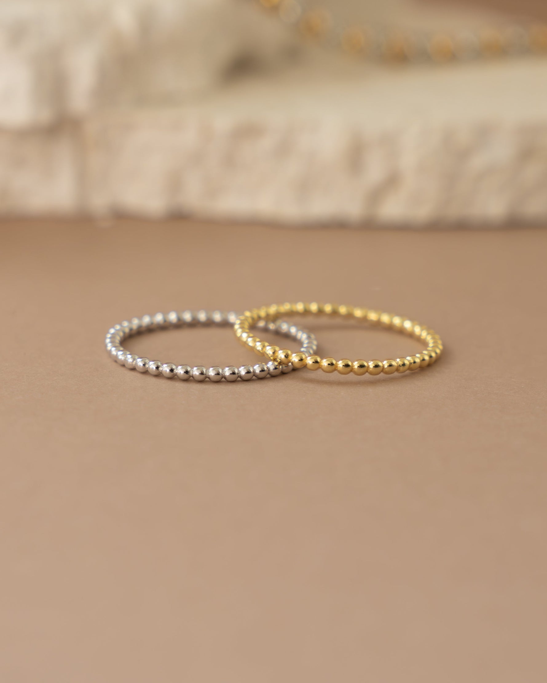 Two gold and silver beaded bracelets on a beige surface