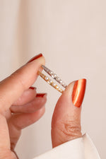 Close-up of a hand holding two 3 pearl rings with a neutral background