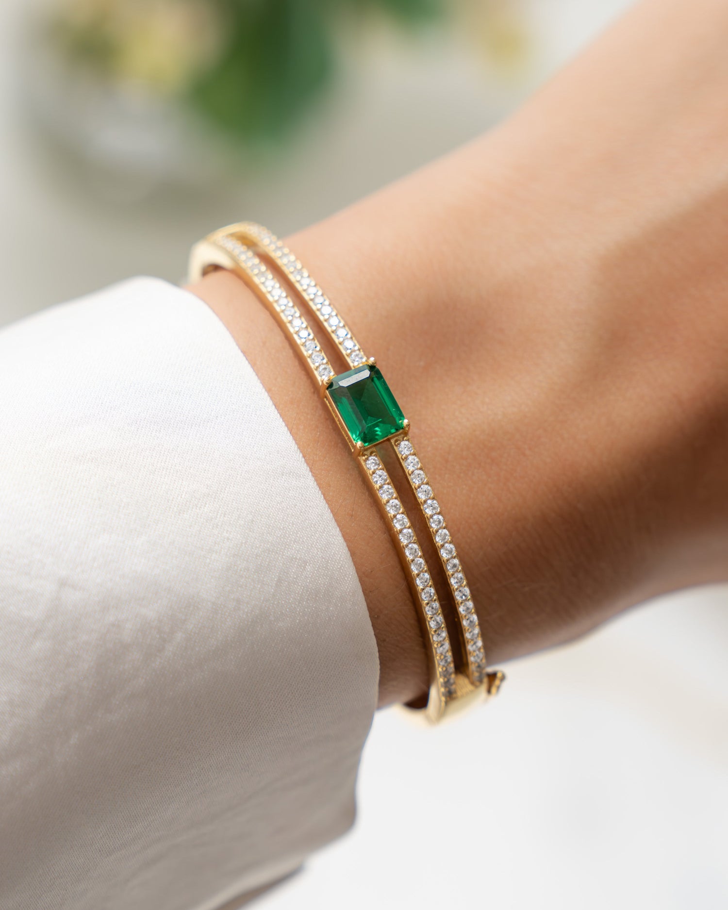 Emerald jewelry featuring a gold bangle on model with a emerald green gemstone and  pave cubic zirconia stones