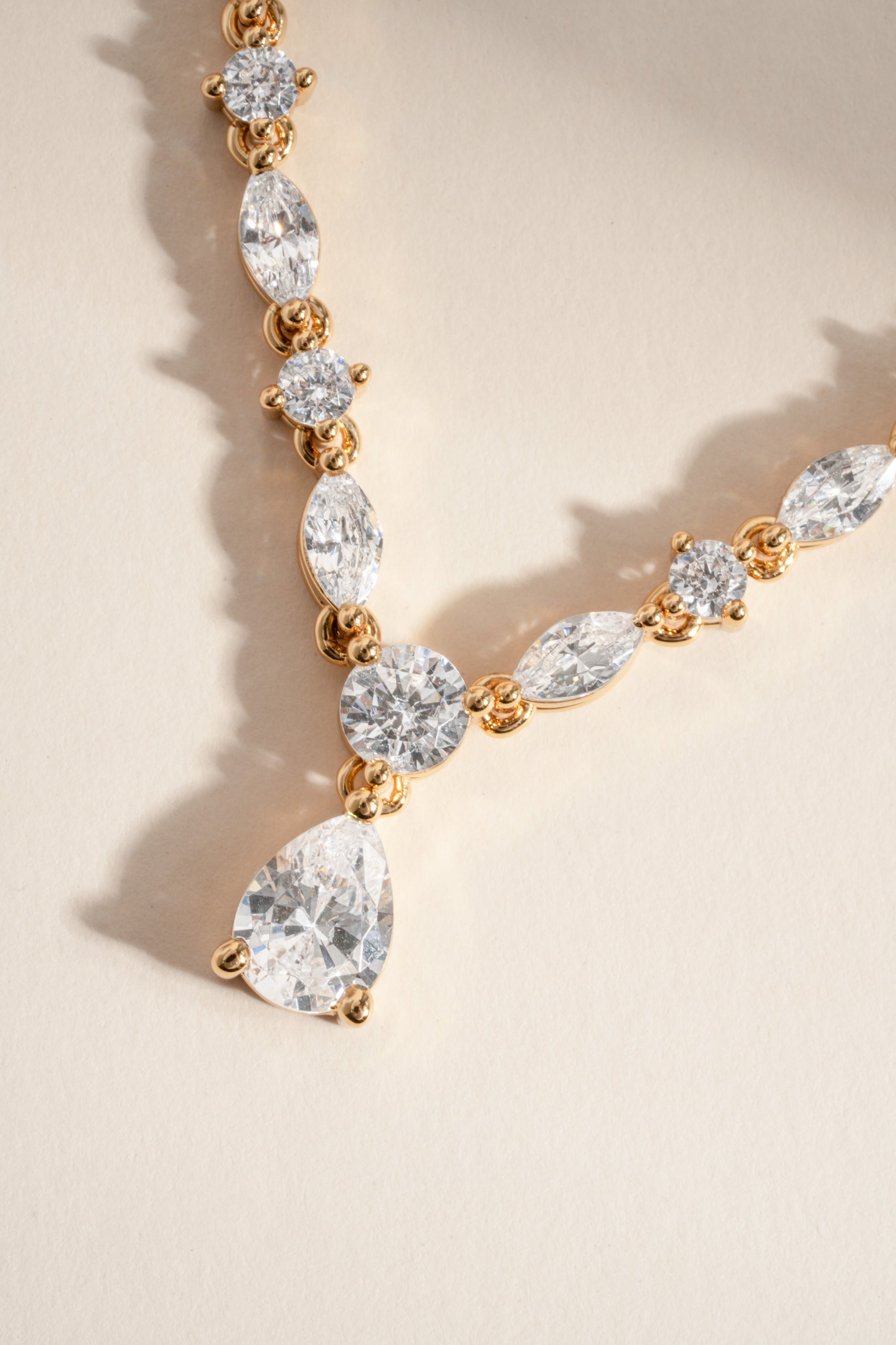 Gold necklace with teardrop-shaped diamonds on a beige background
