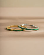 Two gold and silver eternity rings with emerald stones on a beige background
