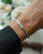 Silver bracelet  on model with a aquamarine gemstone against a blurred floral background