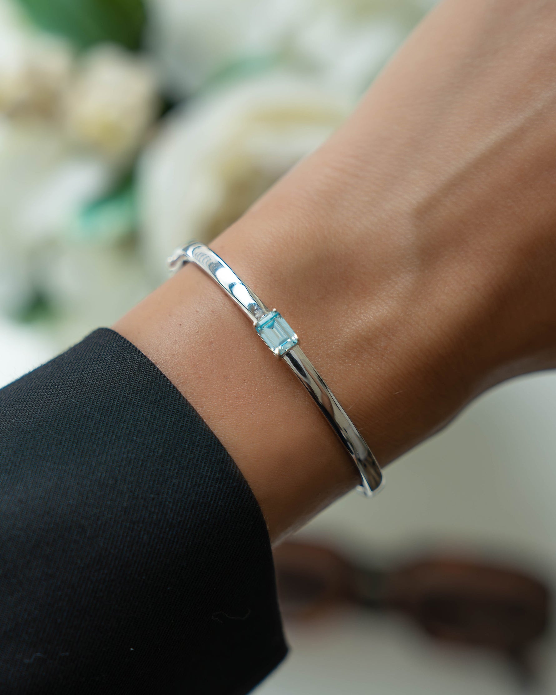 Silver bracelet  on model with a aquamarine gemstone against a blurred floral background