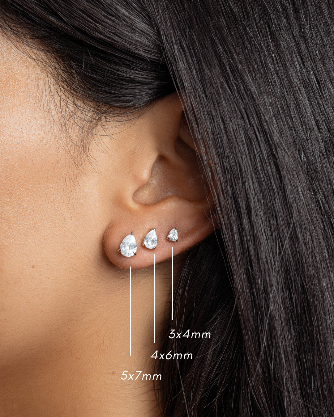 Sterling silver minimalist small earrings with a pear cut cubic zirconia stones featuring a 5x7mm diamond stud earring, a 4x6mm pear cut tiny stud and a 3x4m pear cut diamond dainty earring on models ear 