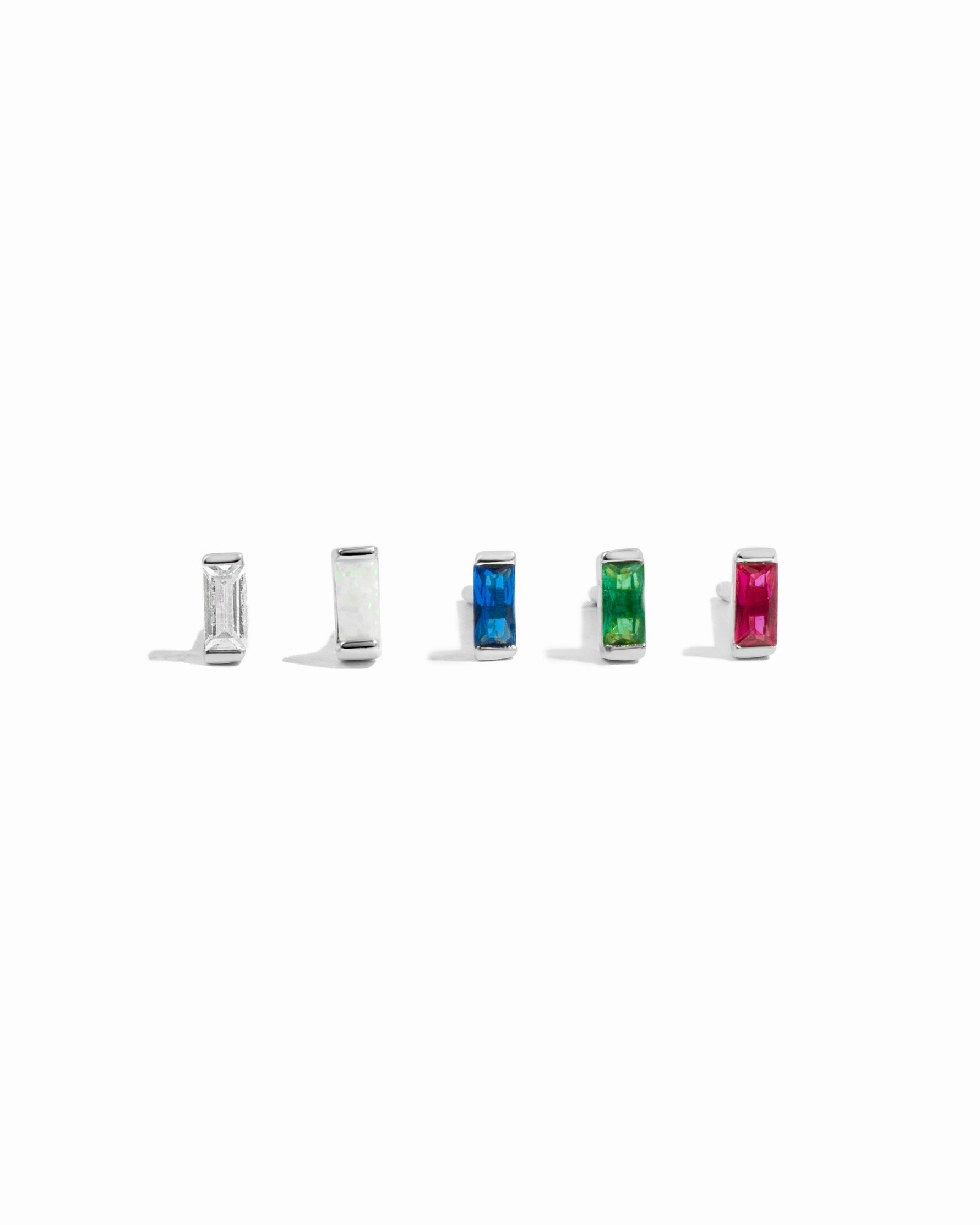 Five small silver studs with different colored stones on a white background featuring white cz, opal, sapphire, emerald, and ruby