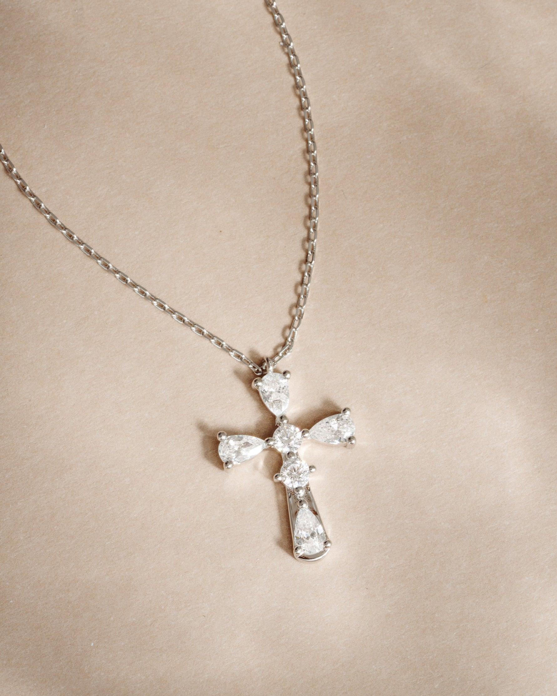 Silver chain cross pendant gemstone necklace on a beige background