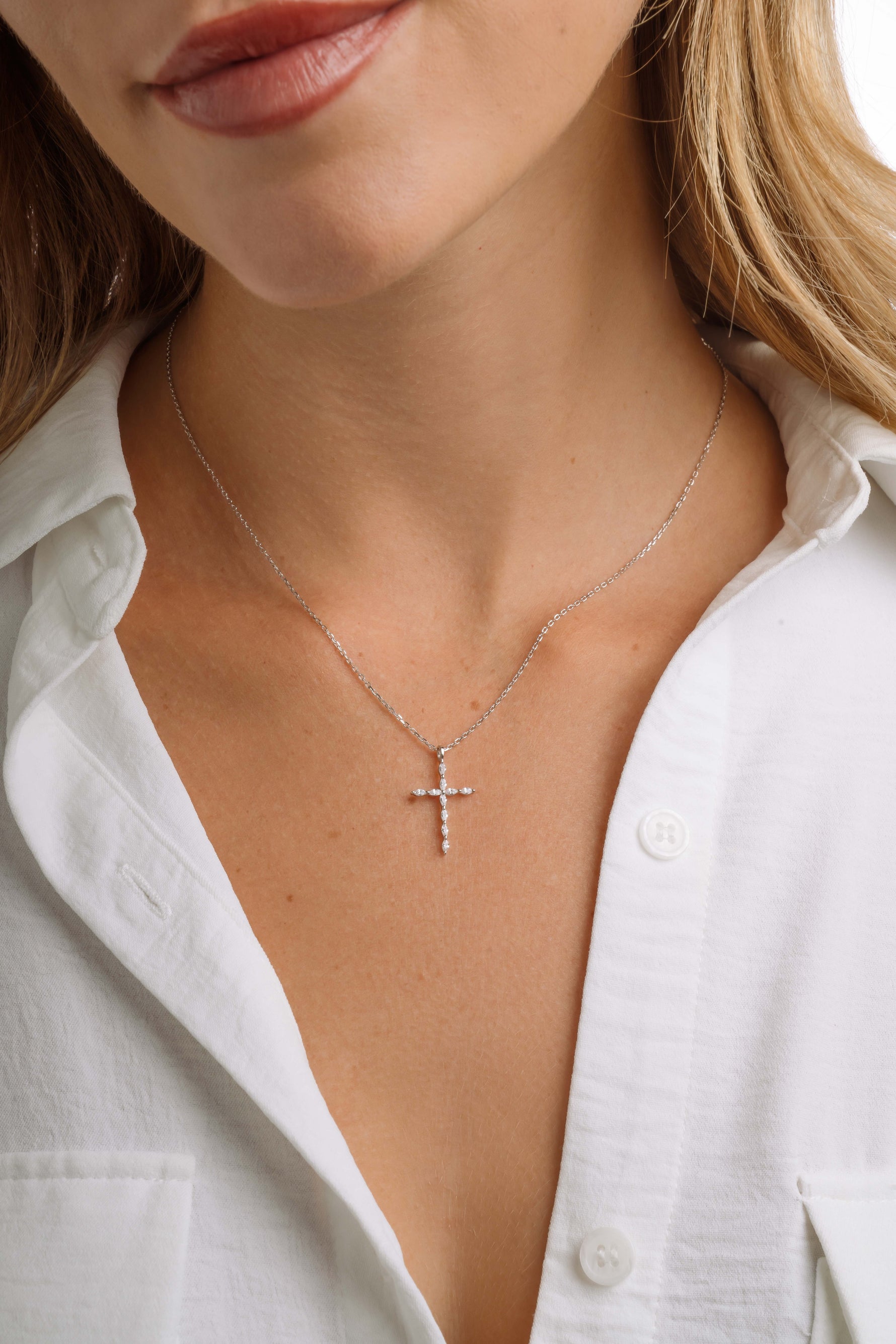 Close-up of a person wearing a sterling silver diamond cross pendant necklace with a white shirt.