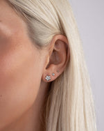 Model wearing sterling silver studs, featuring a flower earring, a small diamond earring, and a gold ball stud earring 