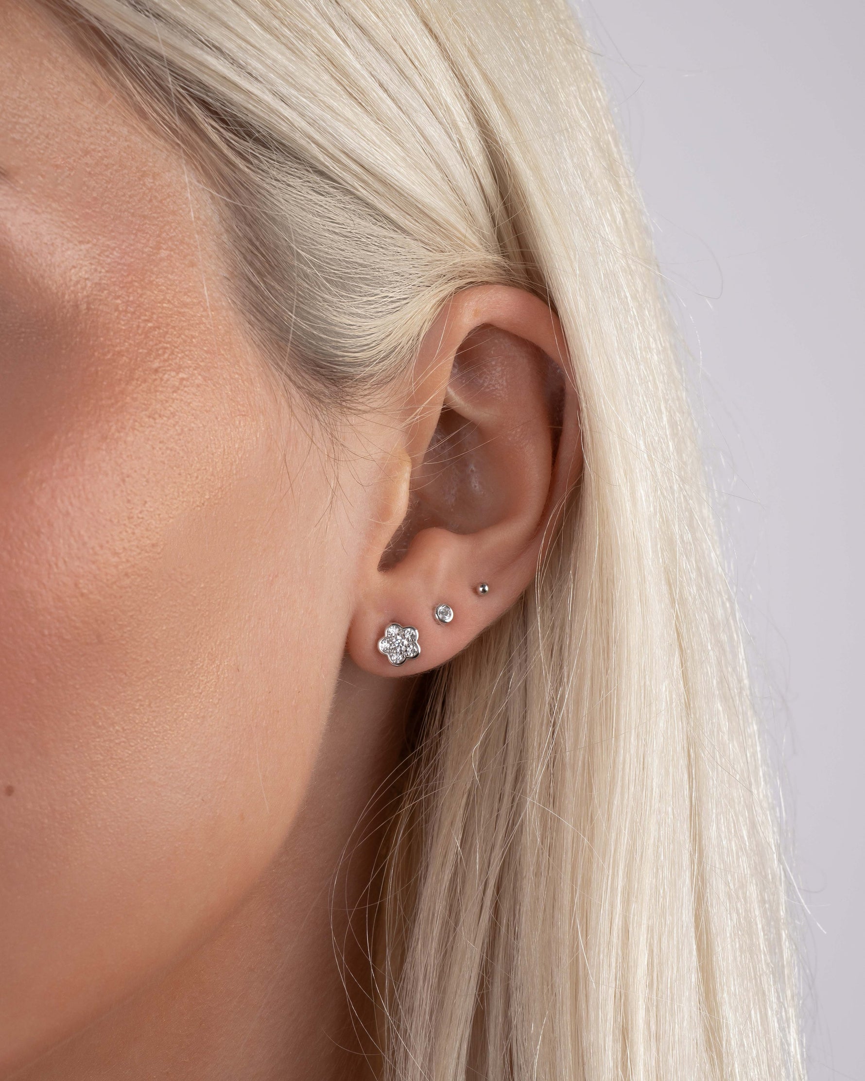 Model wearing sterling silver studs, featuring a flower earring, a small diamond earring, and a gold ball stud earring 