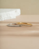 Two diamond wedding band on a beige surface, one gold ring band, and one sterling silver ring band