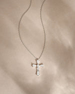 Silver chain necklace with pear cut diamonds with a cross pendant on a beige fabric background