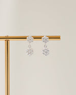 Pair of sterling silver flower earrings on a gold stand against a beige background