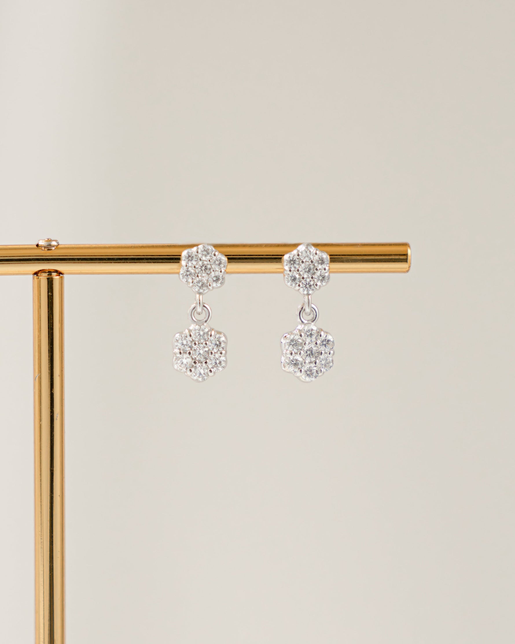 Pair of sterling silver flower earrings on a gold stand against a beige background