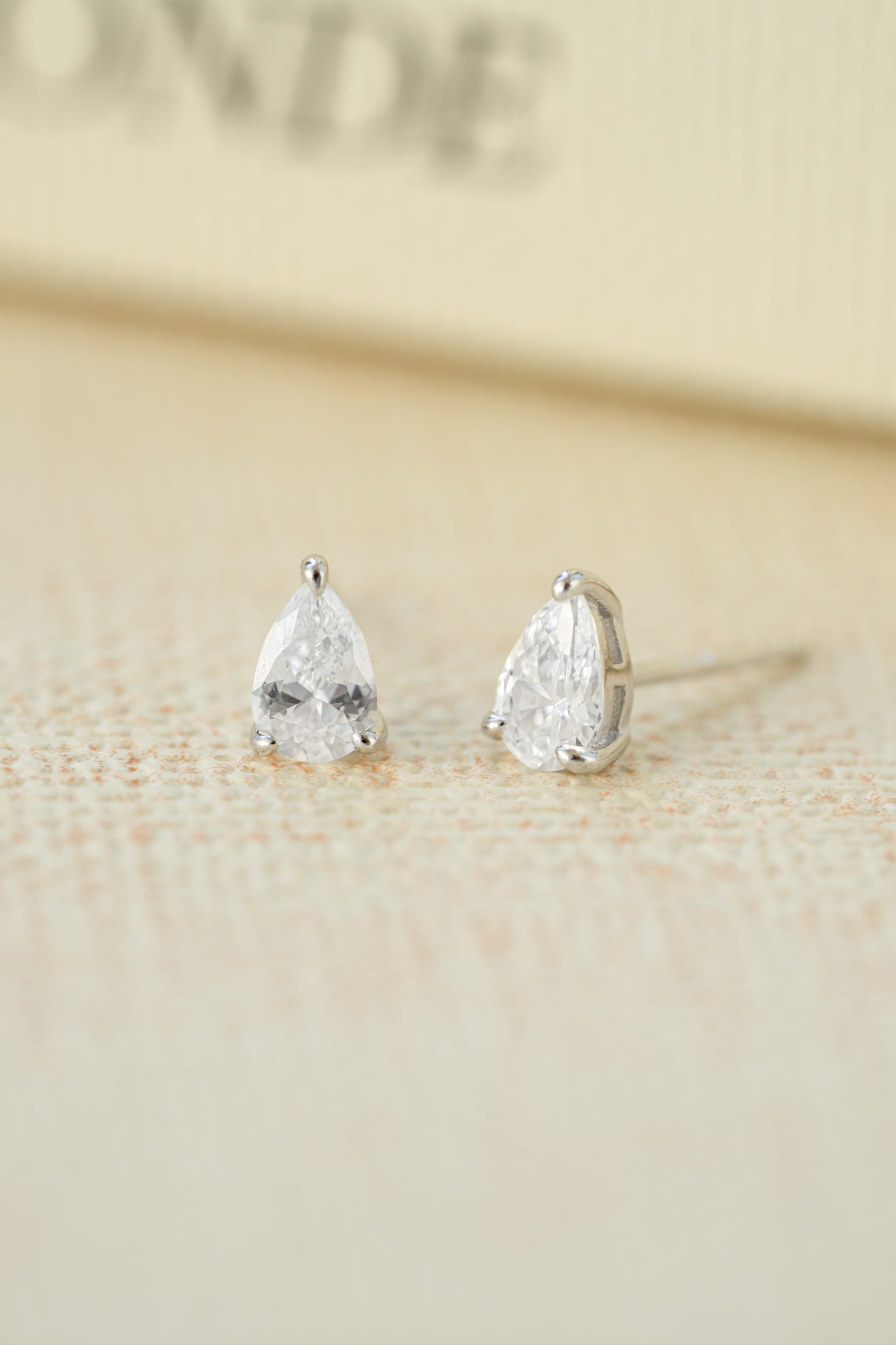 Sterling silver wedding jewelry featuring silver diamond stud earrings on a beige background
