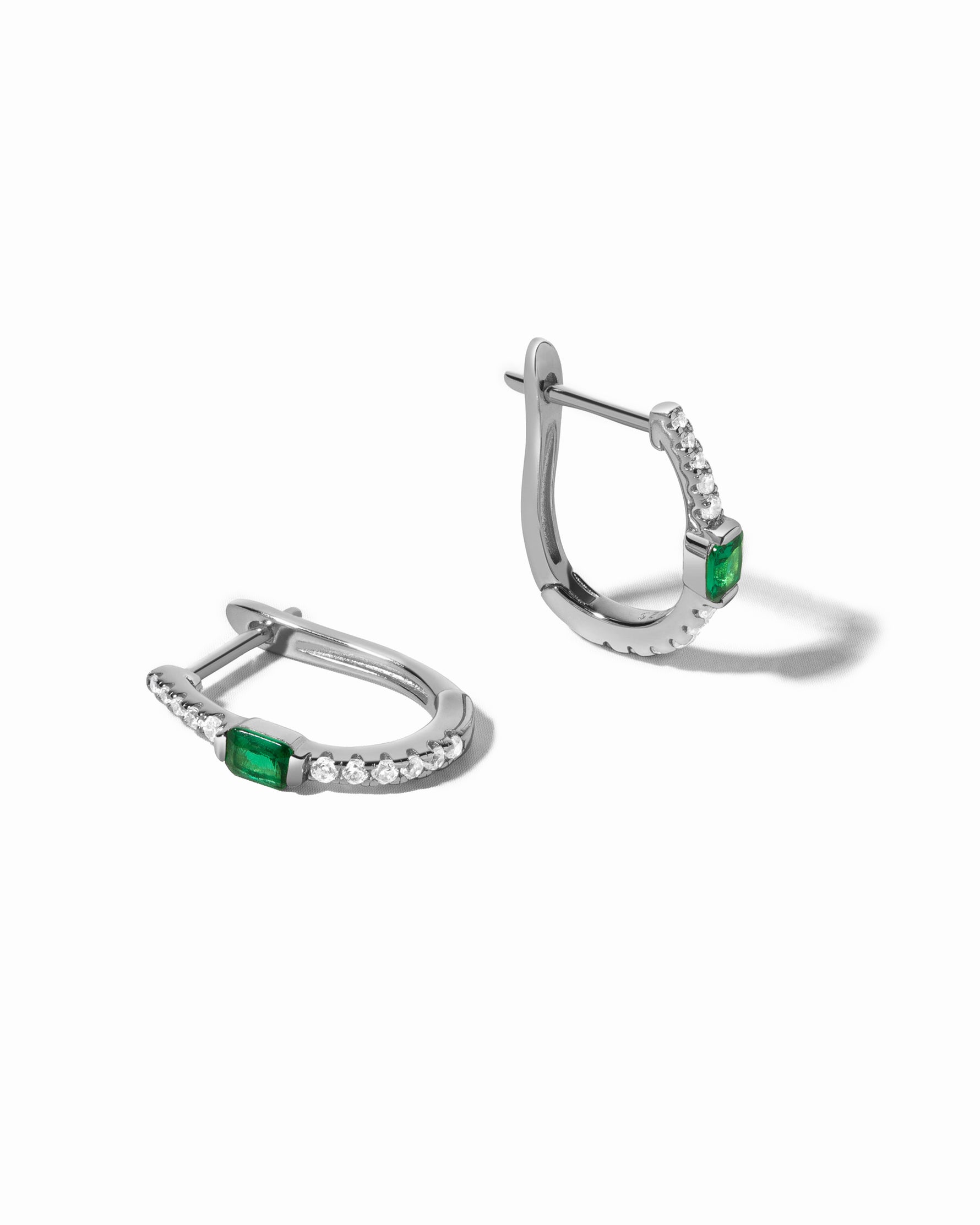 Pair of silver earrings with emerald green gemstones on a white background