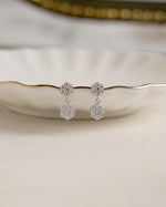 Silver drop earrings with a flower earring design on a decorative plate with a blurred background