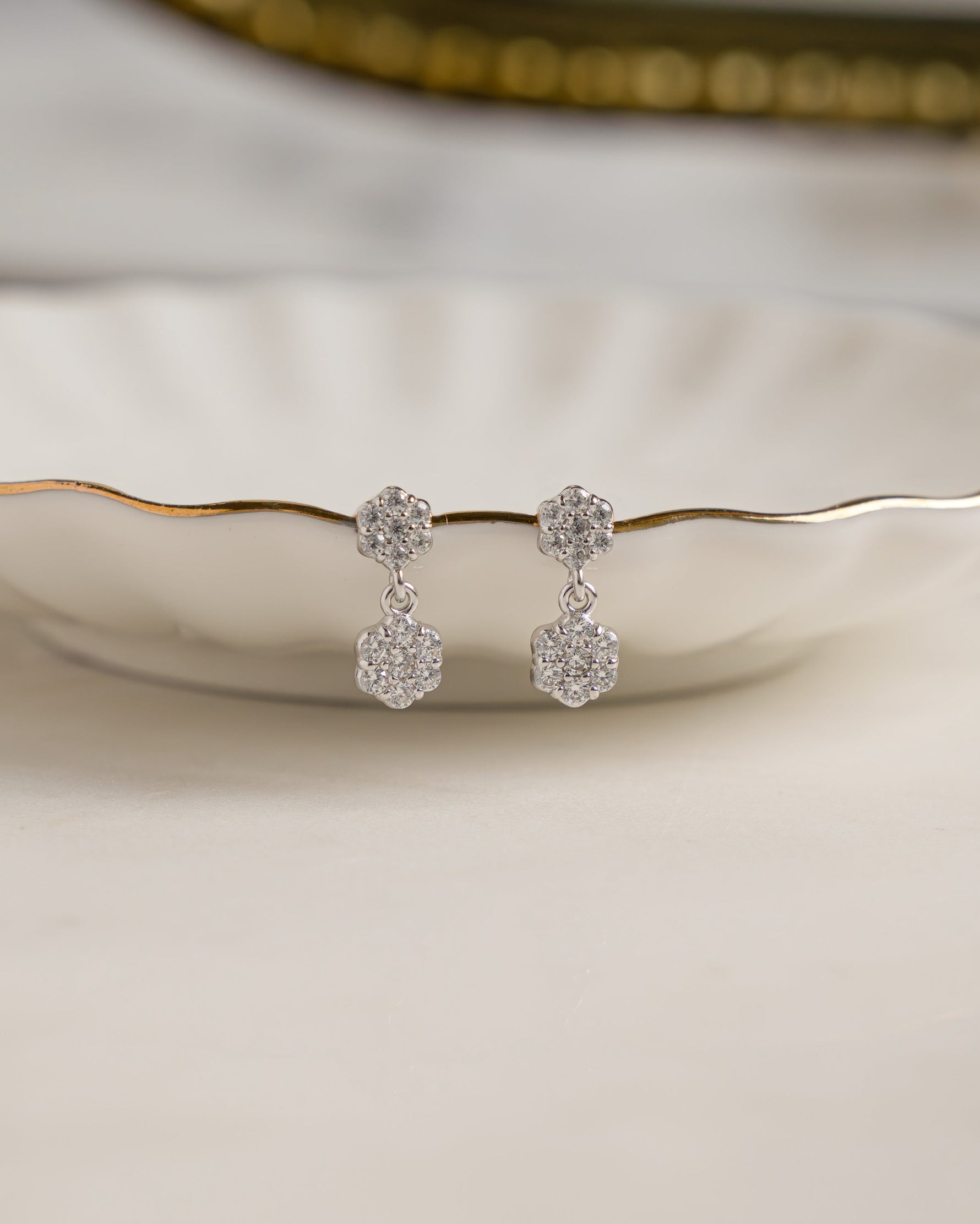 Silver drop earrings with a flower earring design on a decorative plate with a blurred background