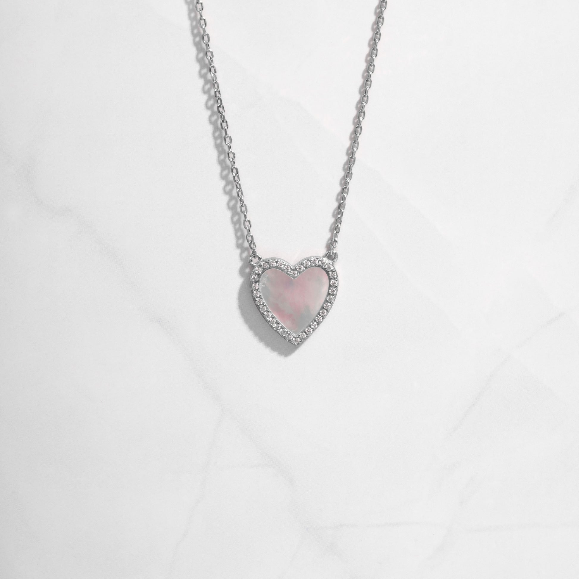 A close-up of the heart necklace showing its radiant mother of pearl surface and delicate  silver chain.