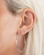 Model wearing 40mm sterling silver hoop earrings, styled with bezel stud and ball stud earrings in a layered ear stack.