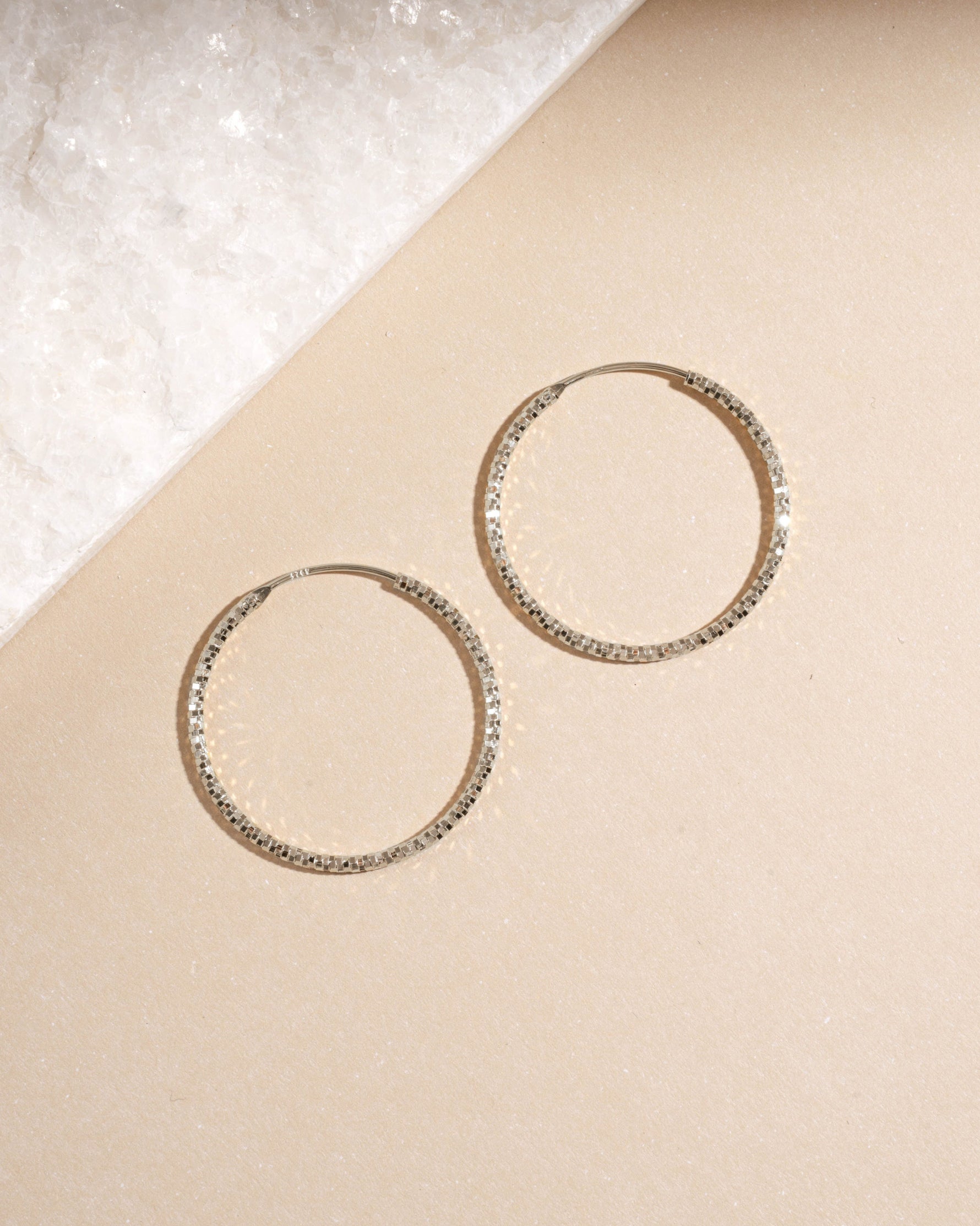 Overhead view of silver 32mm diamond hoops, minimalist earrings and versatile thin hoops for daily wear.