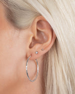 Close-up of silver 32mm hoop earrings on model, styled with delicate stud earrings for a layered, minimalist earring look.