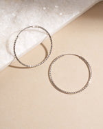Pair of 32mm sterling silver hoop earrings on a beige background, thin and lightweight everyday hoops.