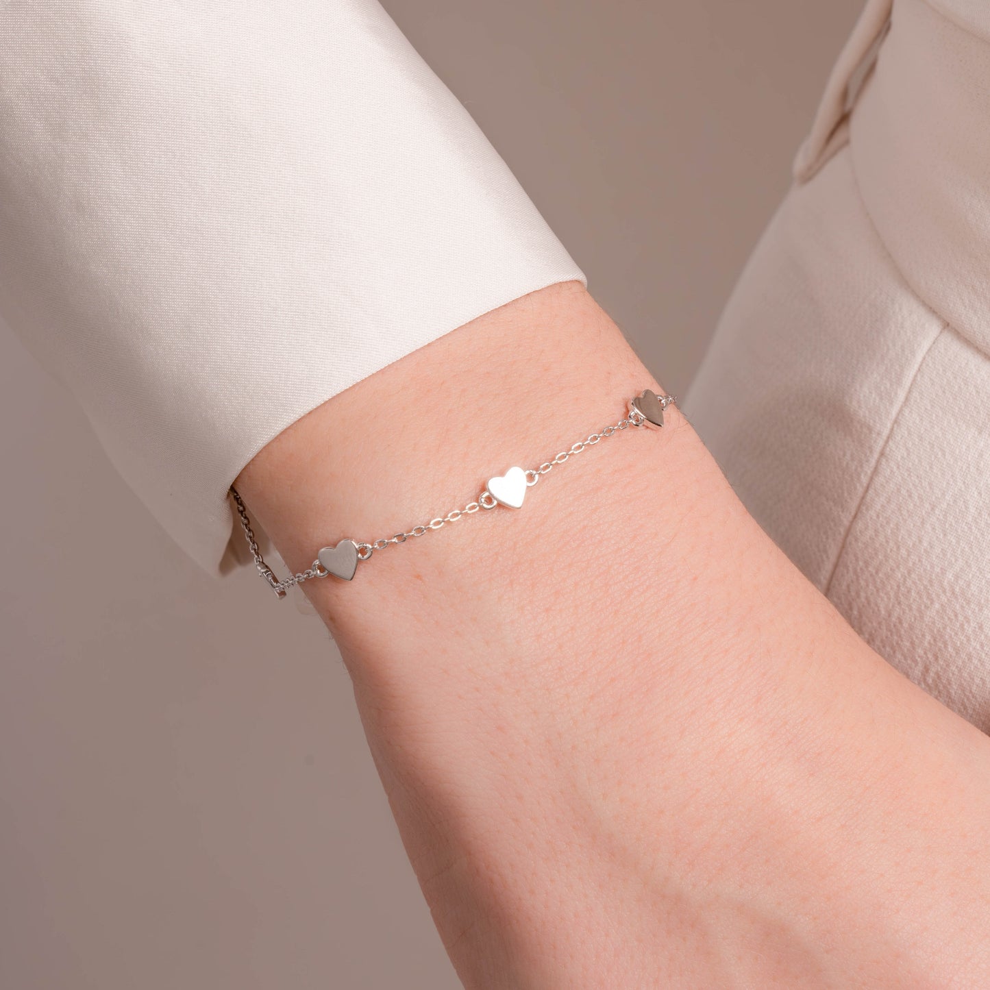 A silver bracelet with heart charms, styled on a model’s wrist, paired with a casual outfit for a minimalist casual look.