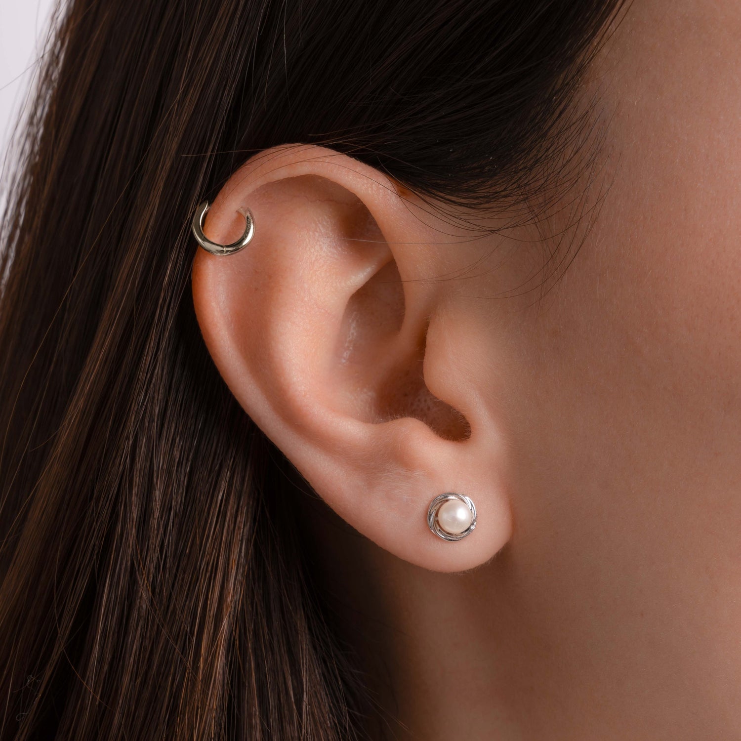 Model wearing dainty pearl stud earrings and a mini hoop in her cartilage