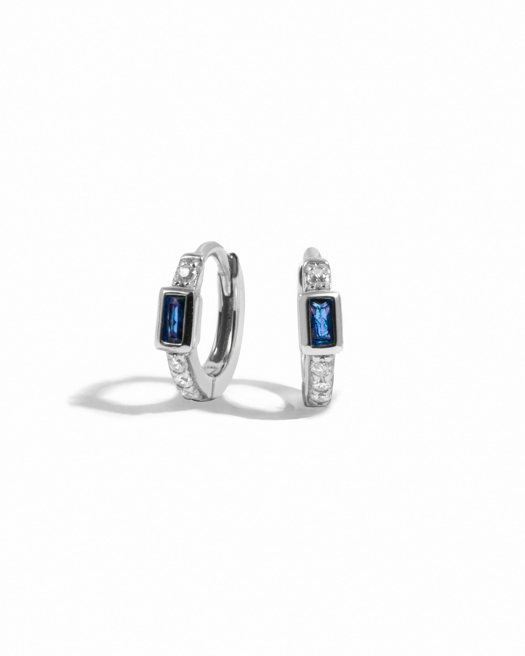 Pair of silver  small hoop earrings with sapphire gemstones on a white background