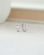closeup image of sterling silver hoop earrings with a baguette cut center stone and two rounded prong setting stones surrounding