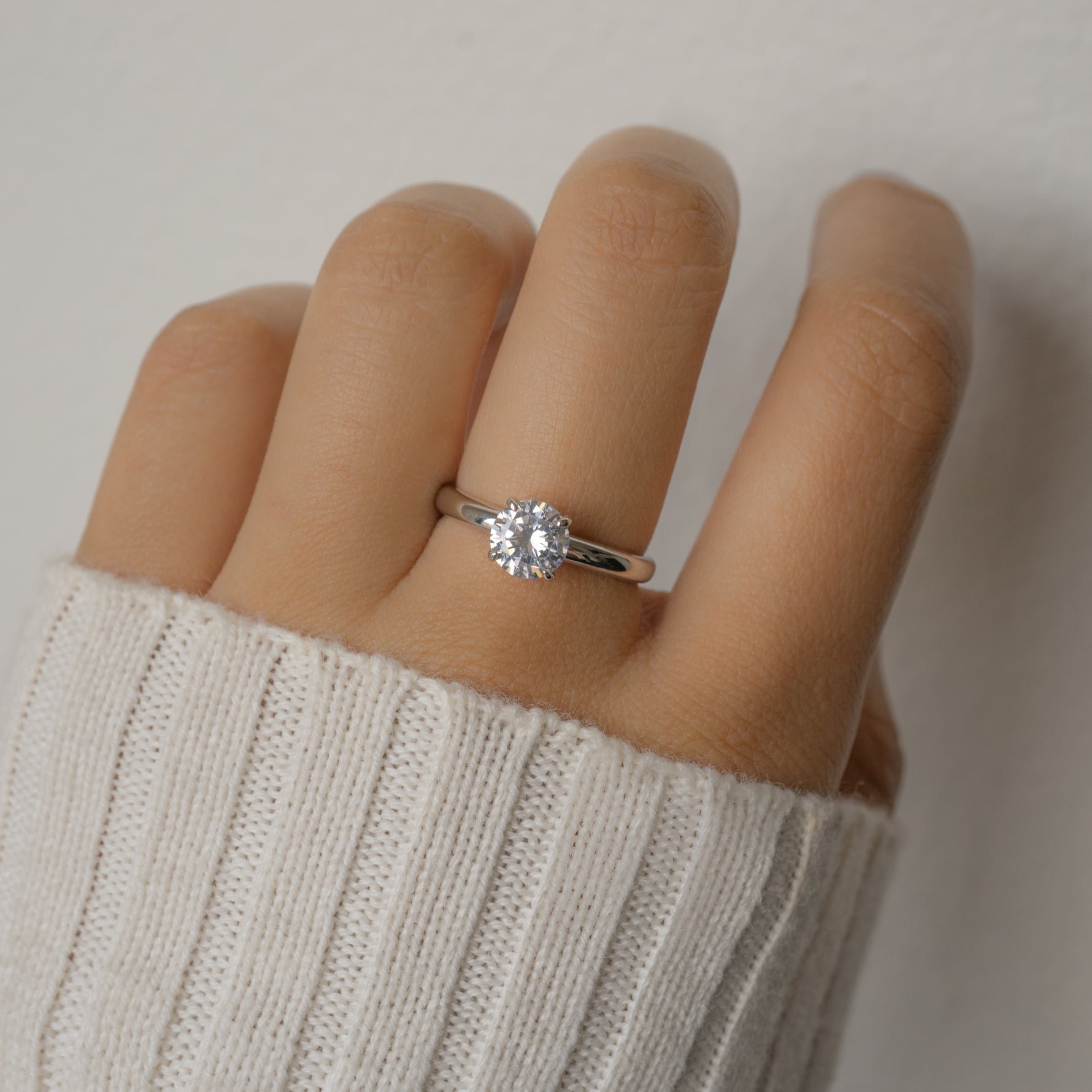 Sterling silver round diamond engagement ring on model's hand.