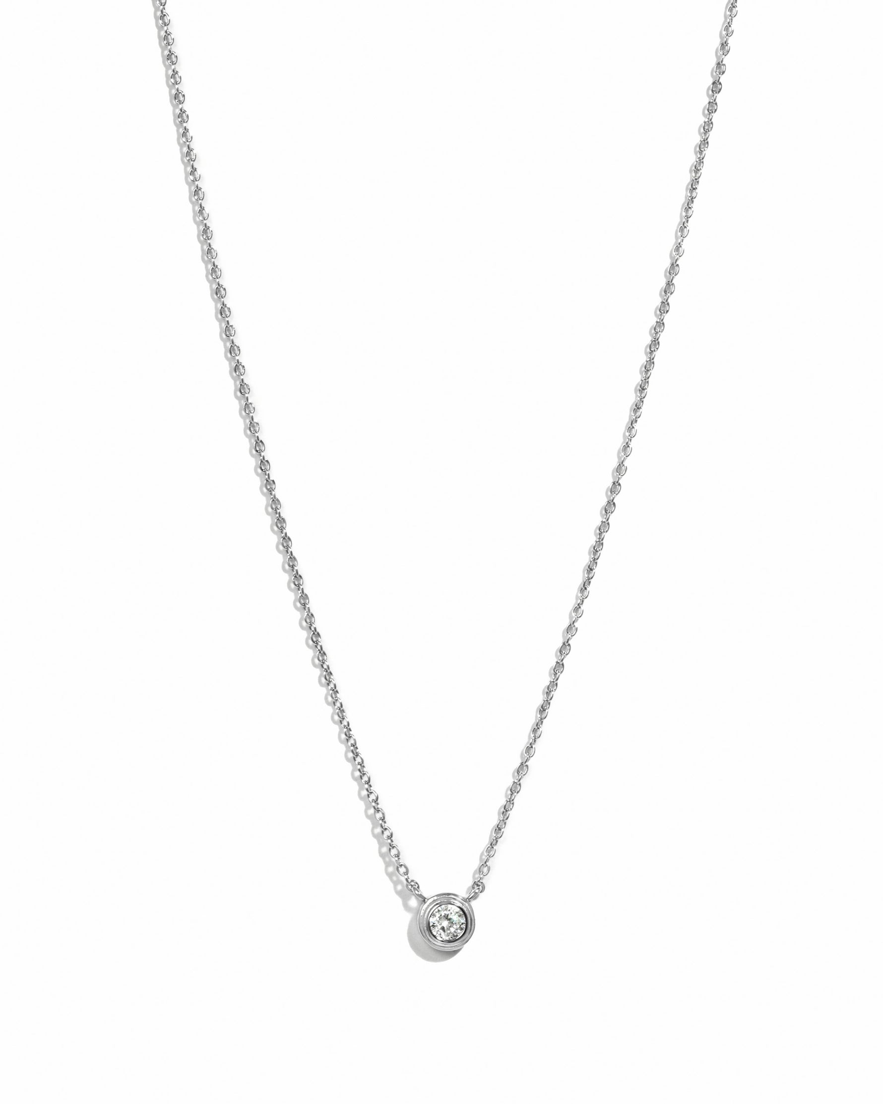 Silver necklace with a small round bezel set diamond pendant on a white background